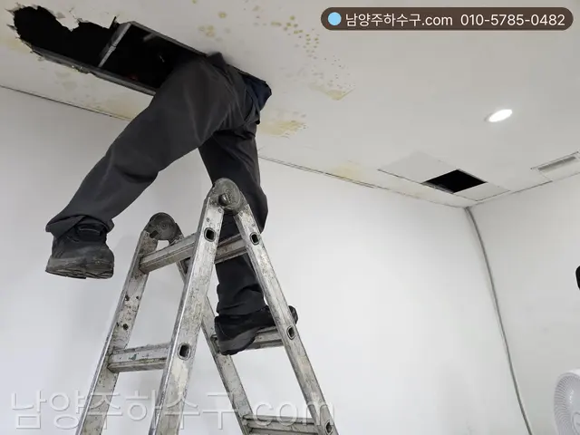 사다리 위에서 천장 점검구 안 드레인 배관을 확인하는 작업